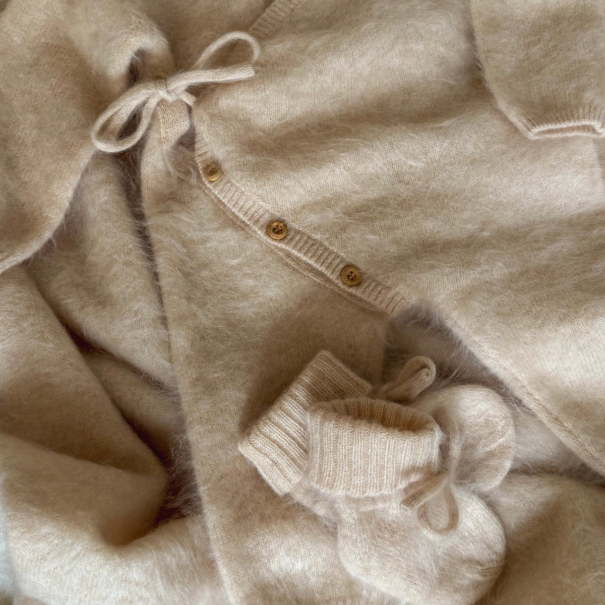 Close-up of cashmere newborn knitwear showing tie fastenings, small buttons and ribbed cuffs.