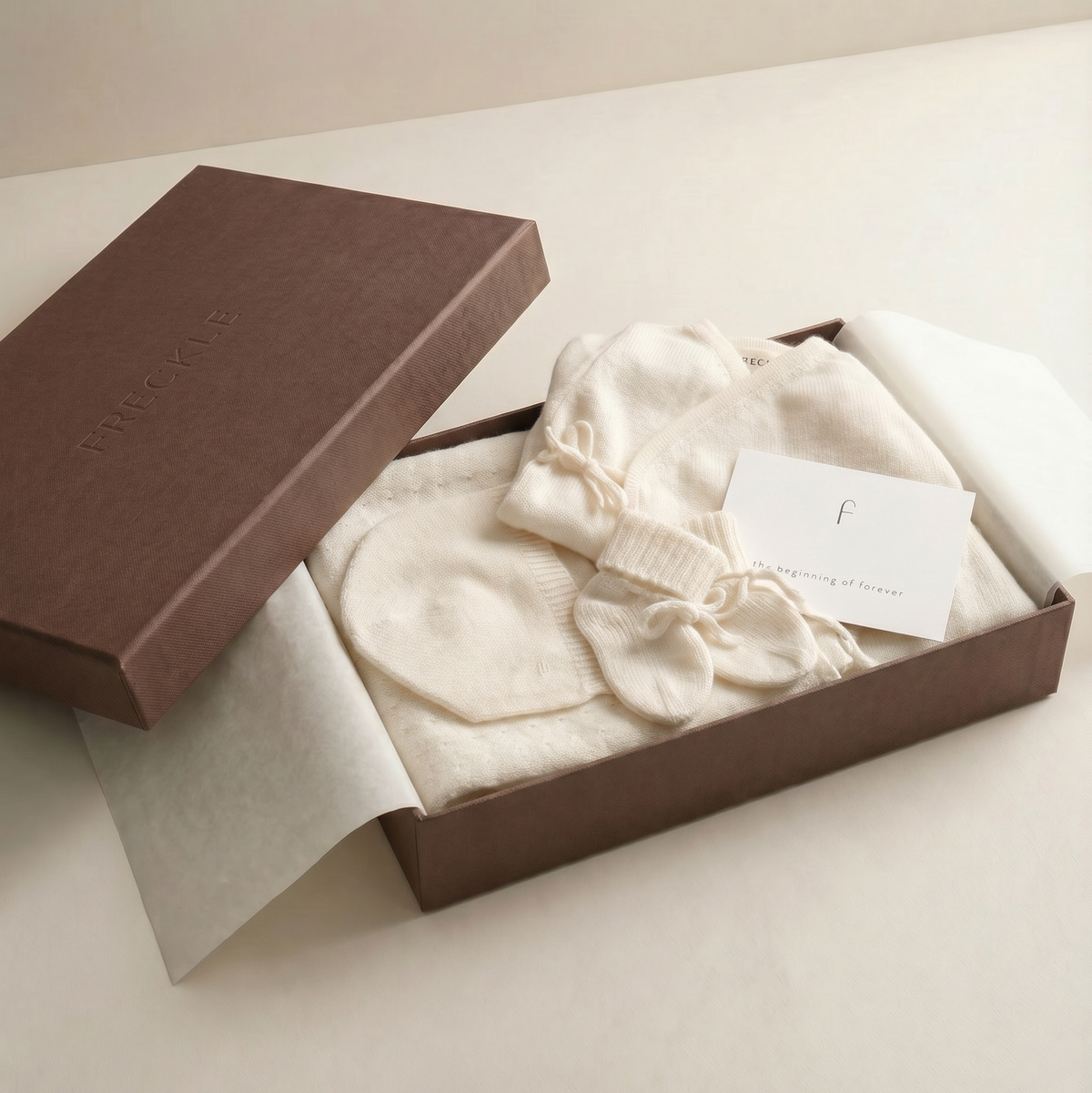Chocolate FRECKLE gift box containing ivory newborn knitwear and fabric packaging.