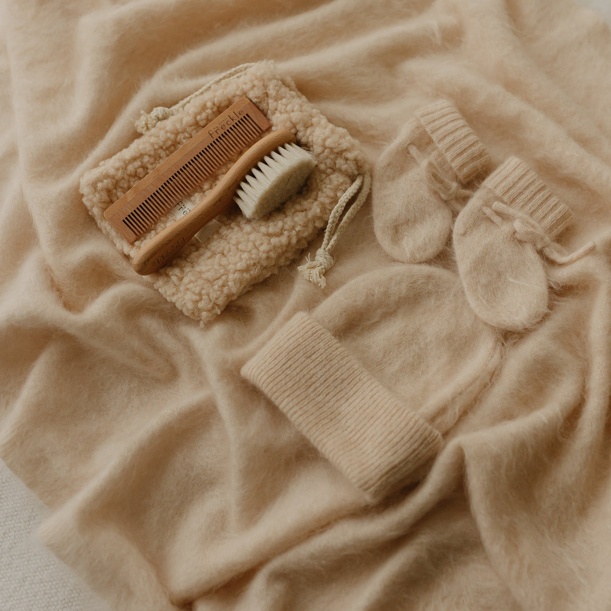 Set of baby grooming tools including a comb and baby hairbrush on a soft beige brushed cashmere blanket gift set