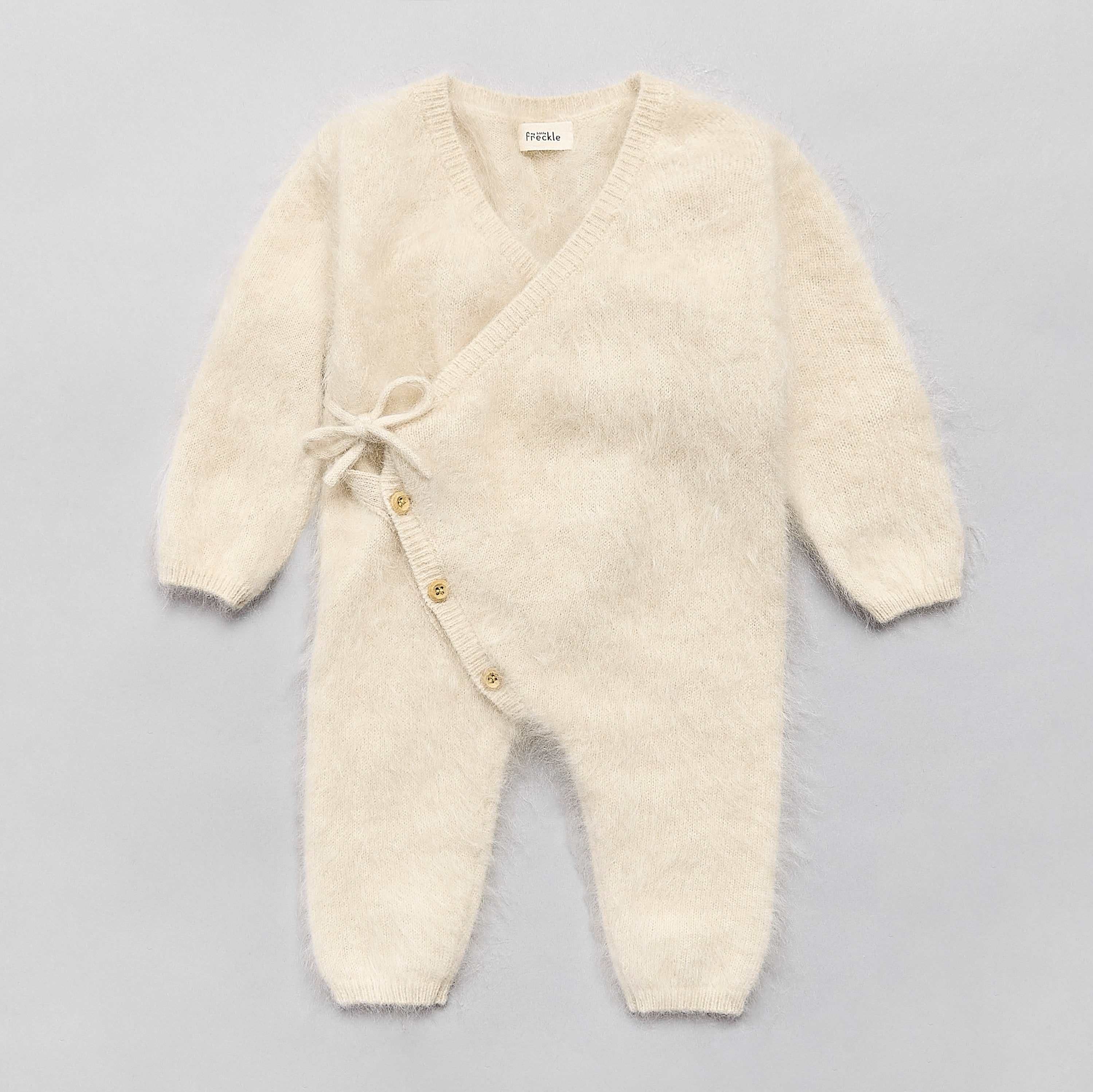 Cream-colored baby brushed cashmere romper with buttons on a grey background