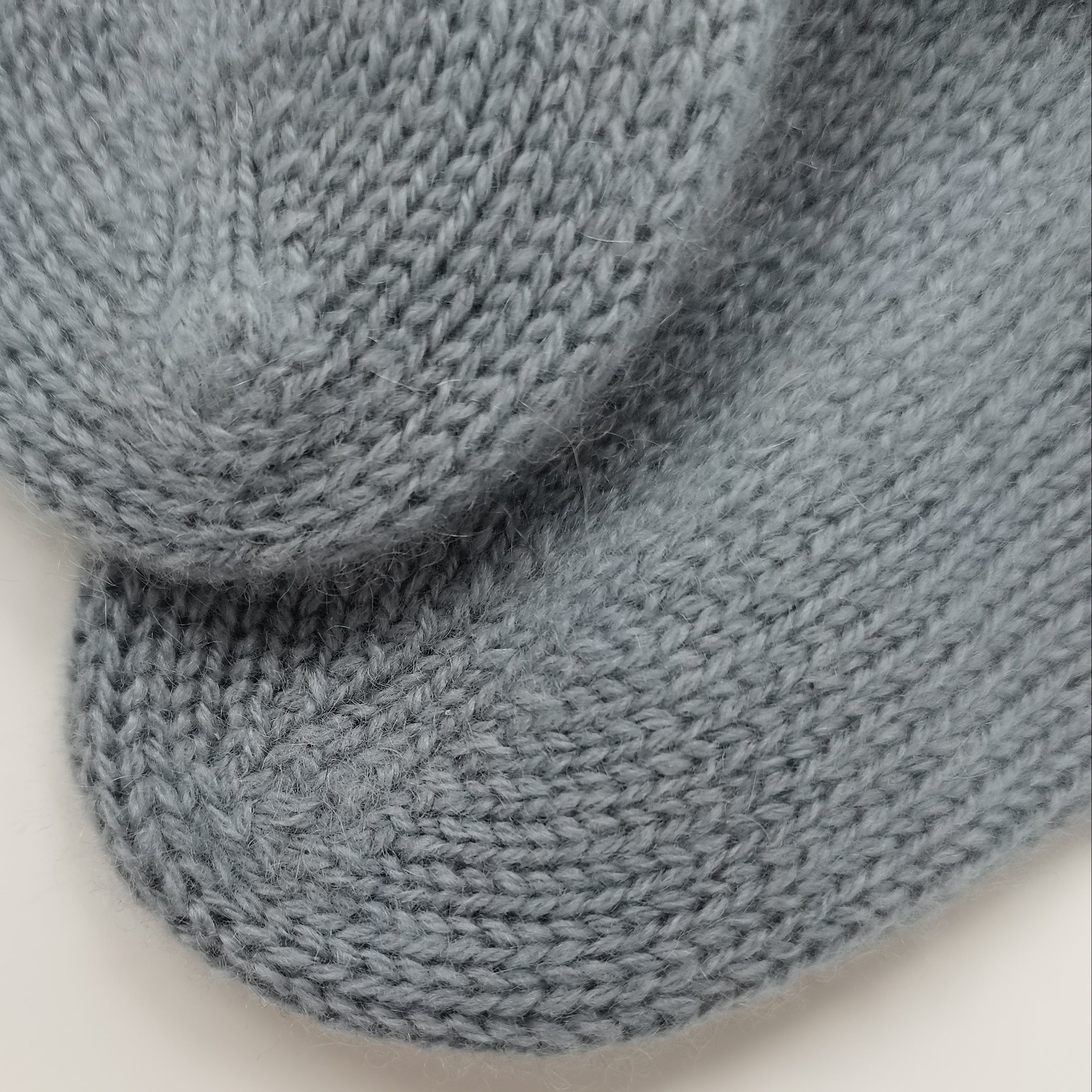 A close-up of a light blue-gray knitted textile, showing the detailed knit texture and curved edges, set against a plain white background.